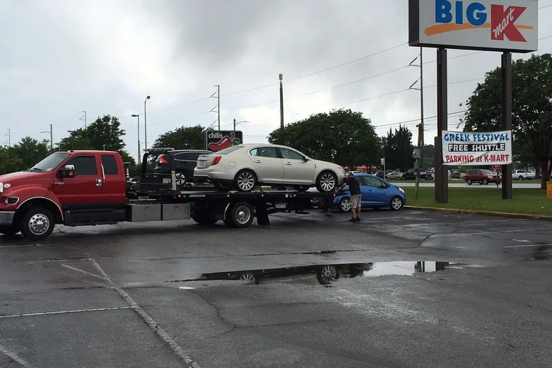 Red flatbed tow truck carrying a sedan, from the existing company website